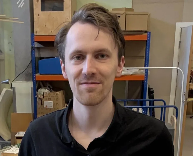 Portrait of Melker Wändahl, creator of Tilt Tracker, standing in a workshop with shelves of parts behind him.