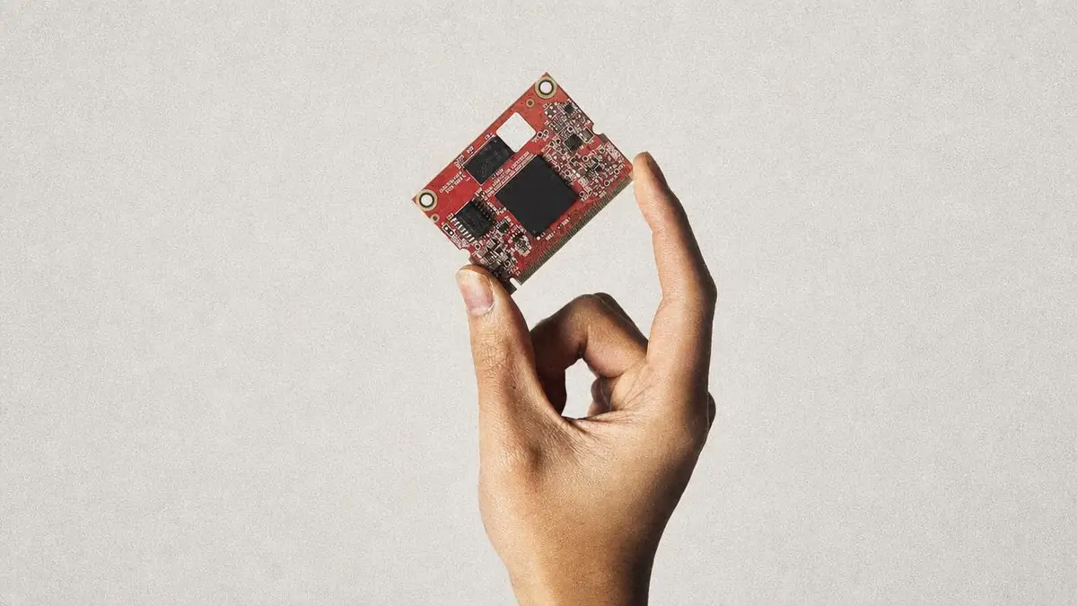 A hand holding a small red printed circuit board module
