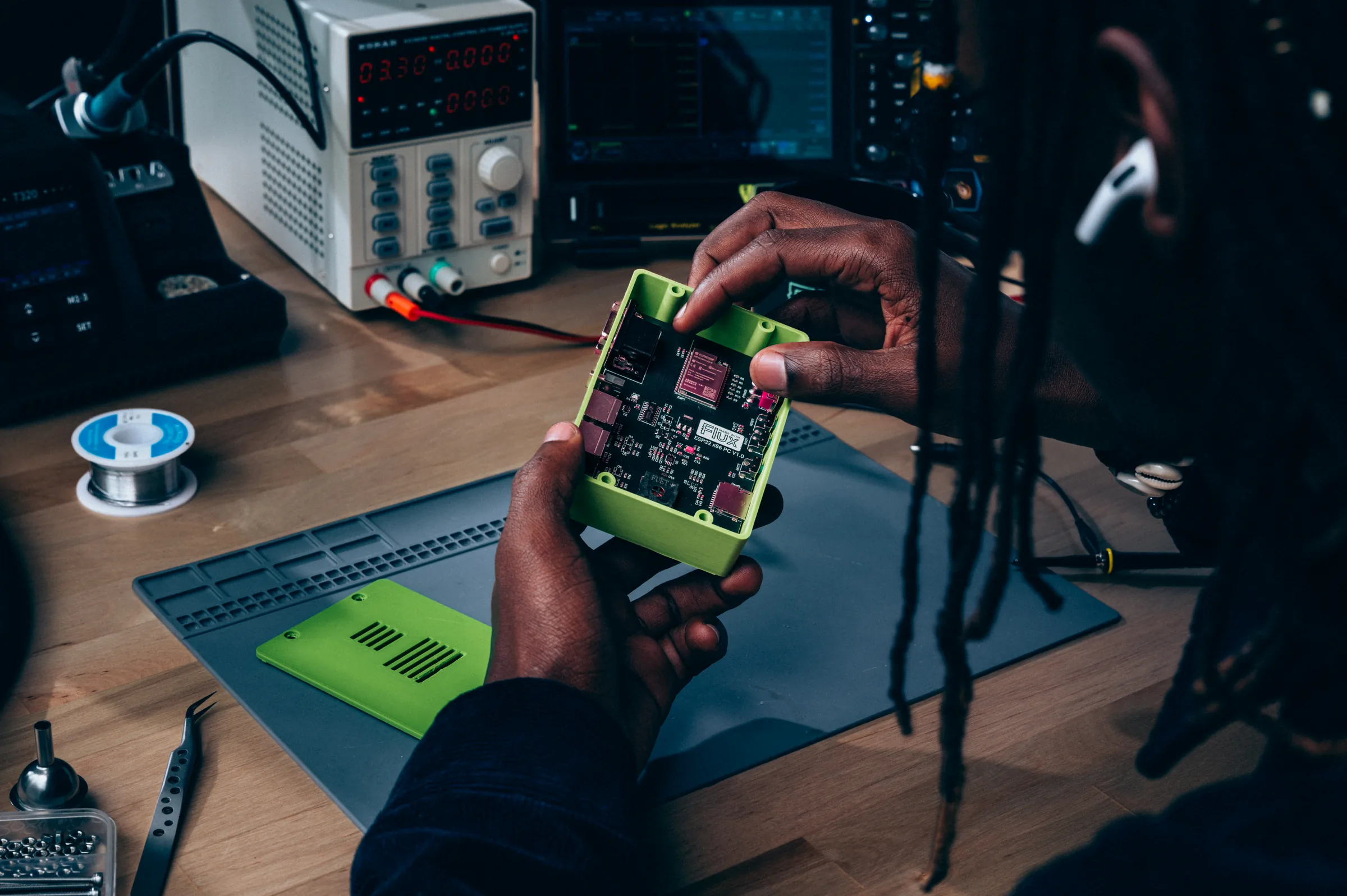 An engineer holds a board in a green enclosure at the bench