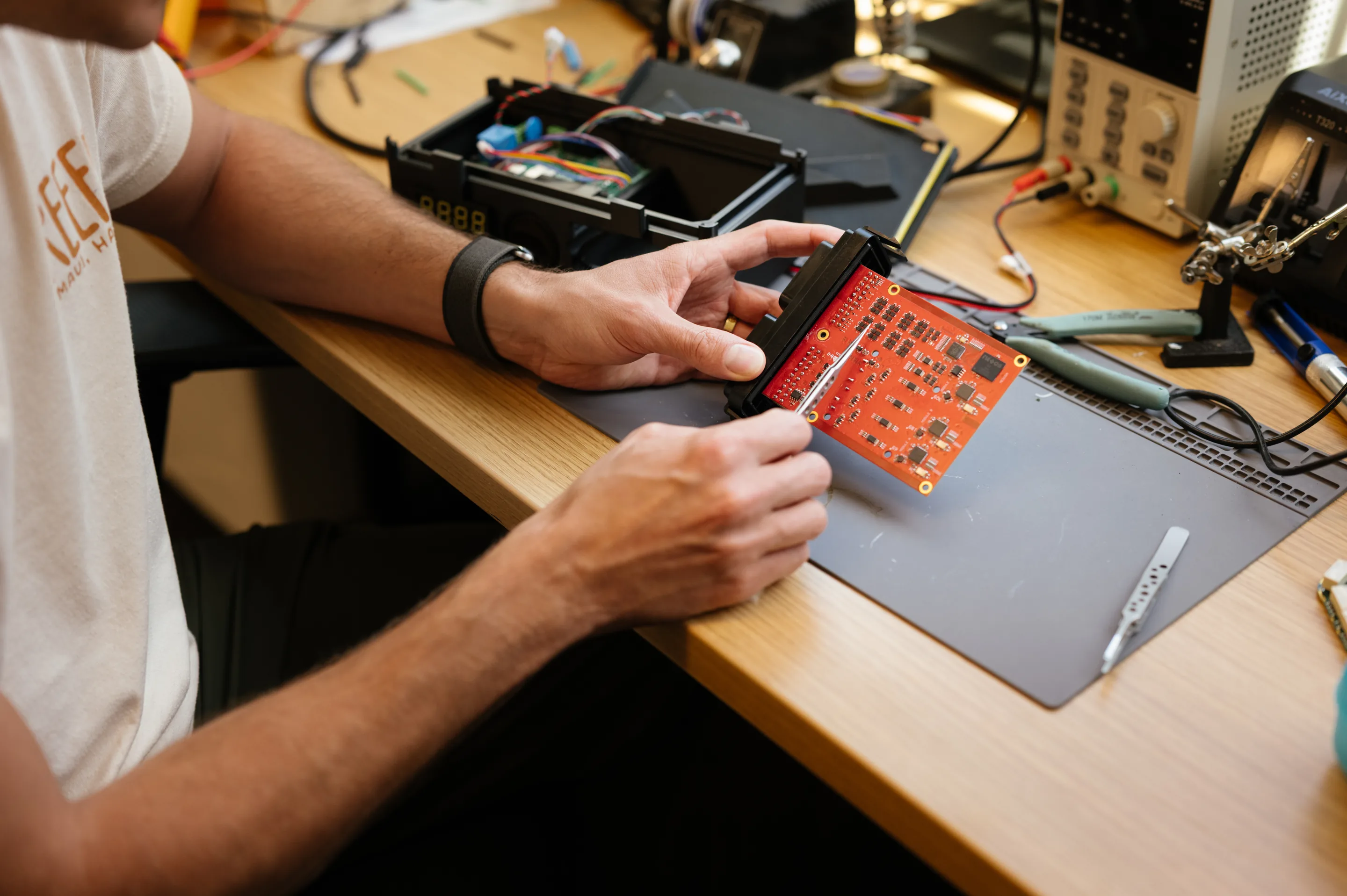 Hands measure a red circuit board with a caliper at the bench